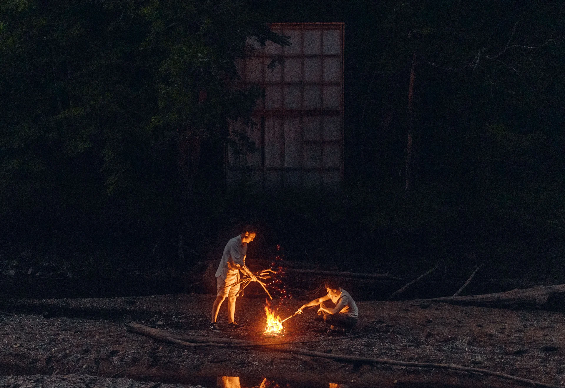 Vue frontale de nuit du projet depuis l'autre rive de l'Aix, deux personnes allument un feu dans le lit de la rivière