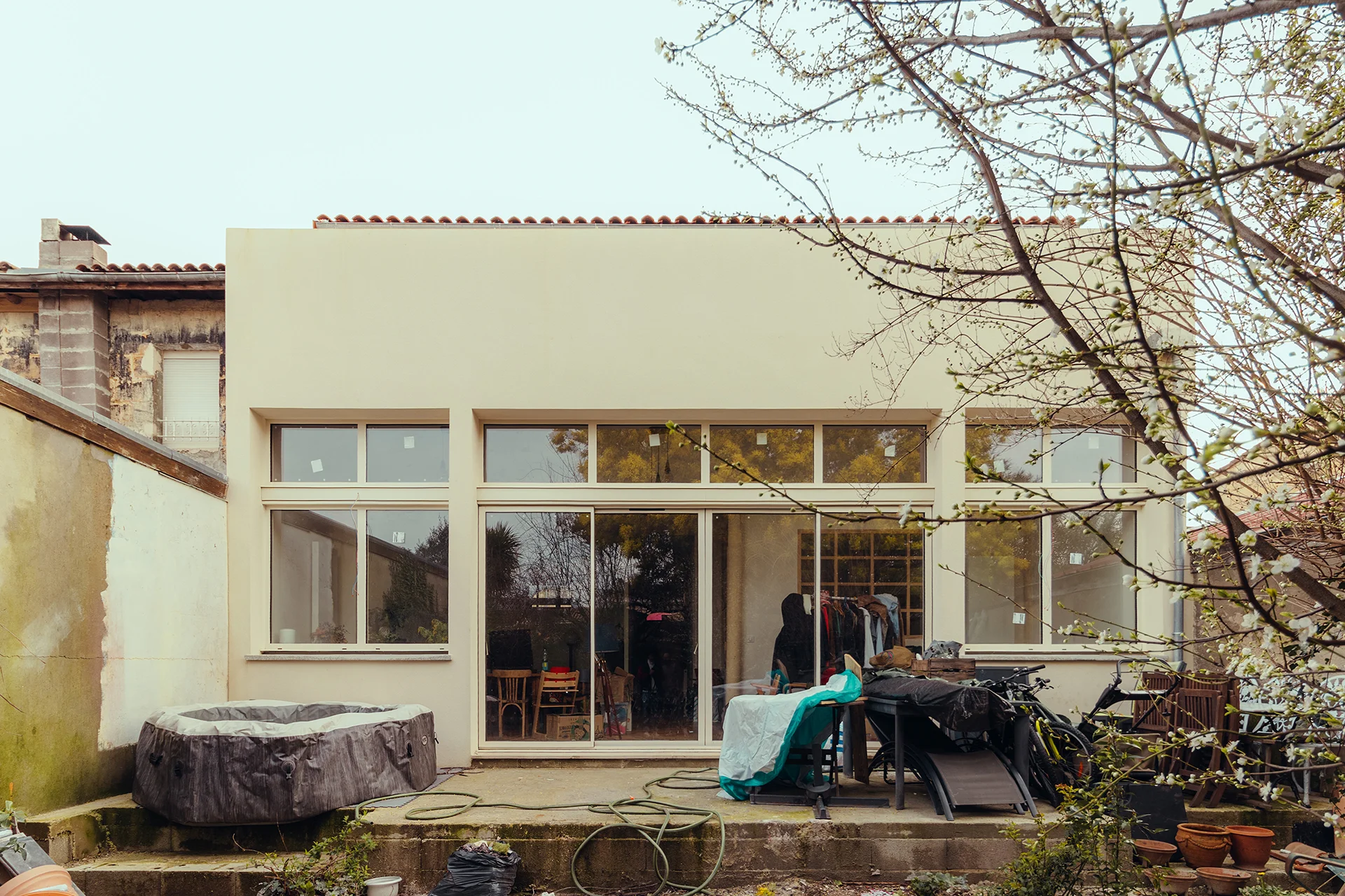 Vue de la façade arrière avec sa grande baie double hauteur, 4 ouvrants sur terrasse, linteau, maçonnerie et enduit ton pierre, menuiserie en alu couleur beige