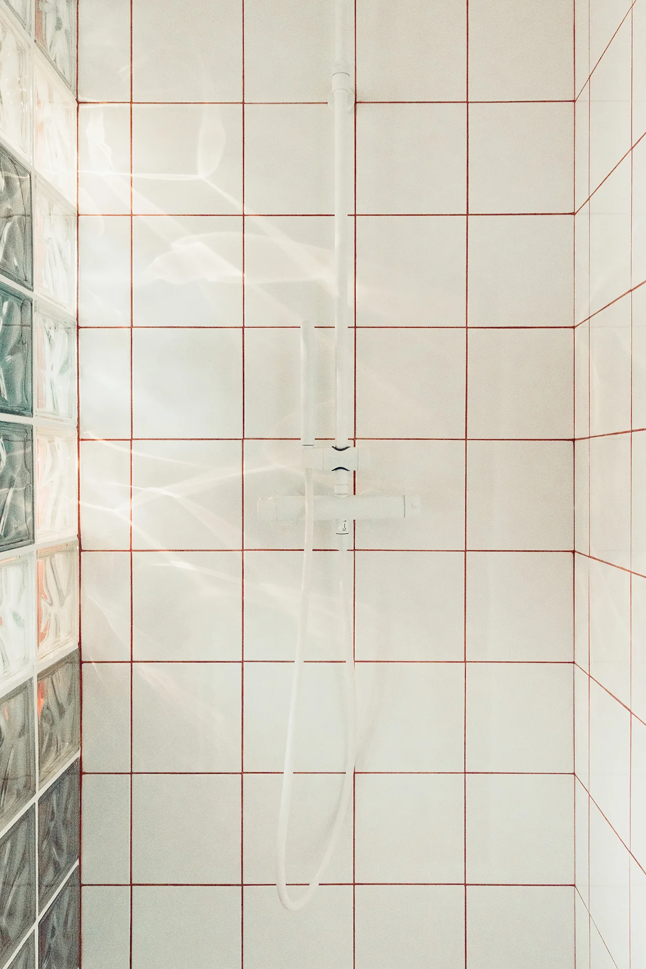 Cabine de douche en négatif du reste (carrelage blanc joints terracotta), colonne de douche blanc mat, éclairage intégré à la douche depuis le caisson en bois